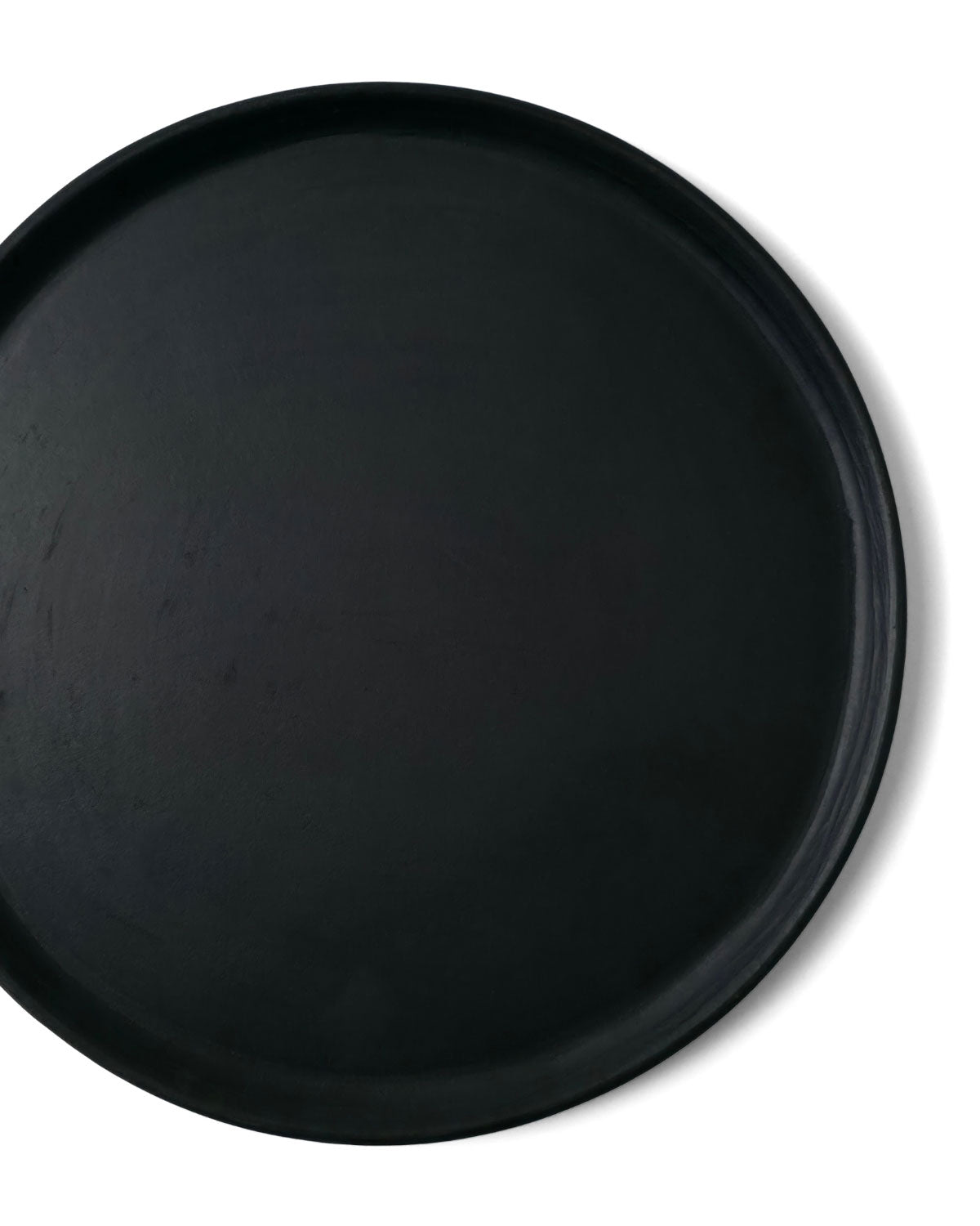 Close-up top view of Oaxacan black clay dinner plate showing raised rim on white background.