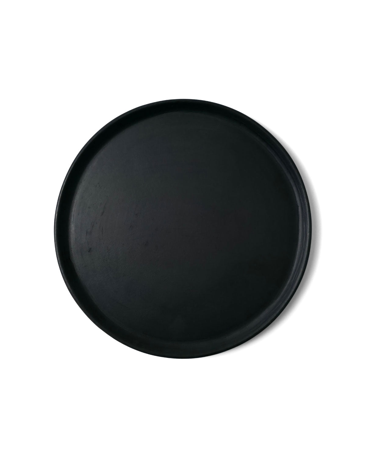Top view of matte Oaxacan black clay dinner plate on white backdrop.