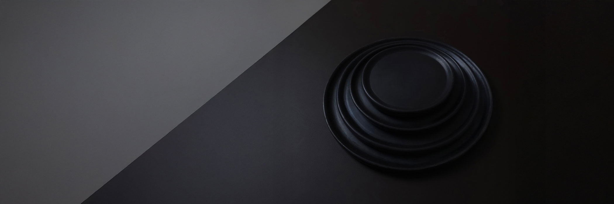 Wide banner showing stacked Oaxacan black clay dinner plates on dark diagonal backdrop.