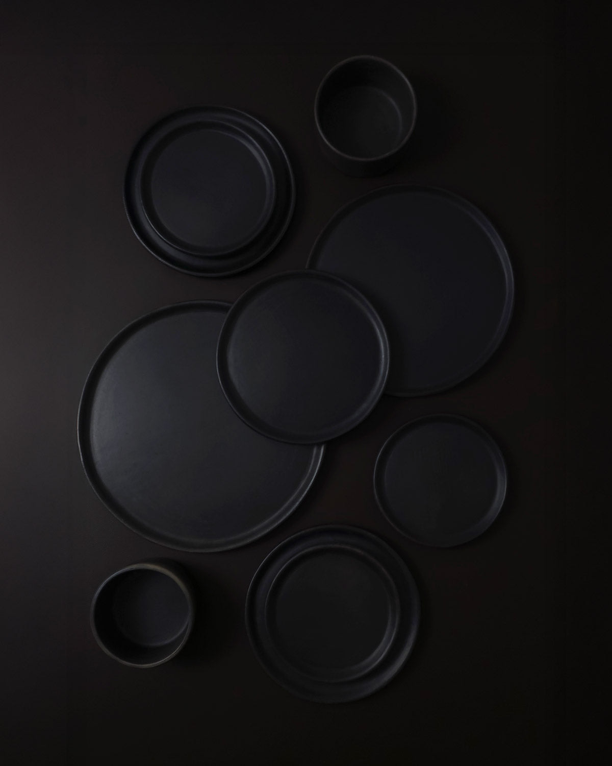 Flat-lay of assorted Oaxacan black clay dinnerware—including plates and a bowl—arranged on a dark backdrop.