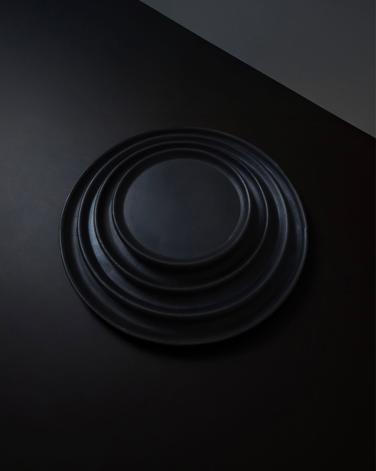 Stacked set of matte Oaxacan black clay plates on dark background.