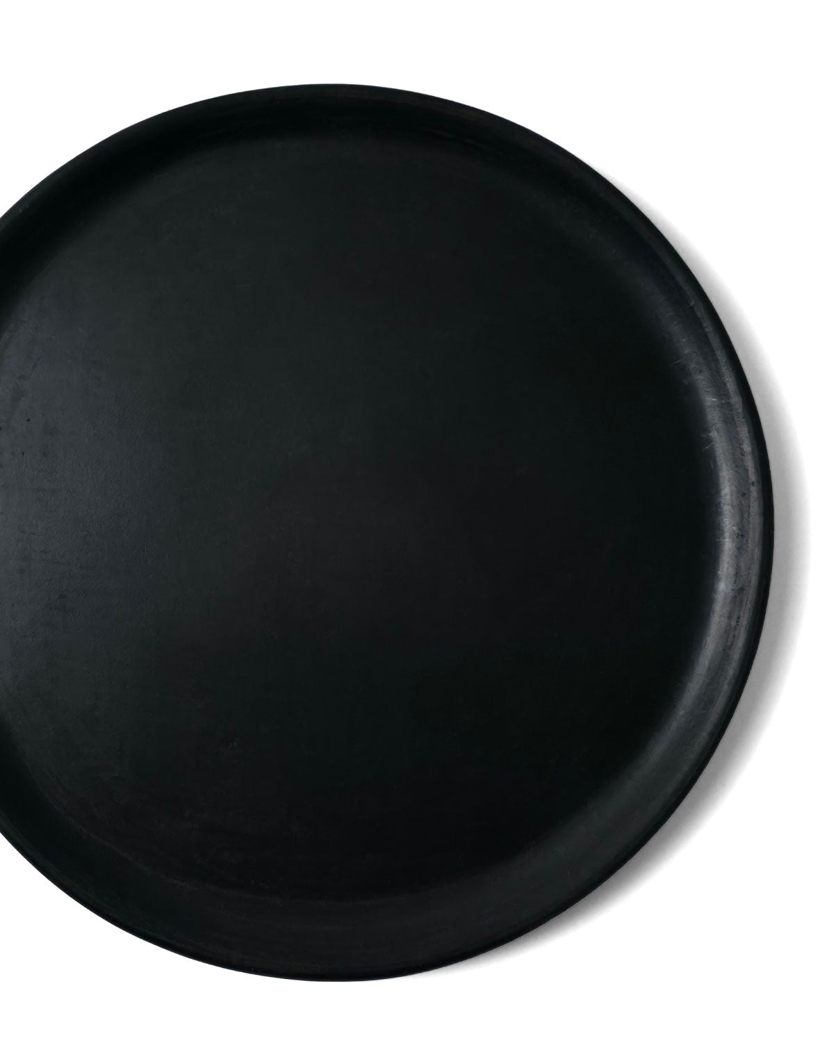 Close-up top view of Oaxacan black clay salad plate showing raised rim on white background.
