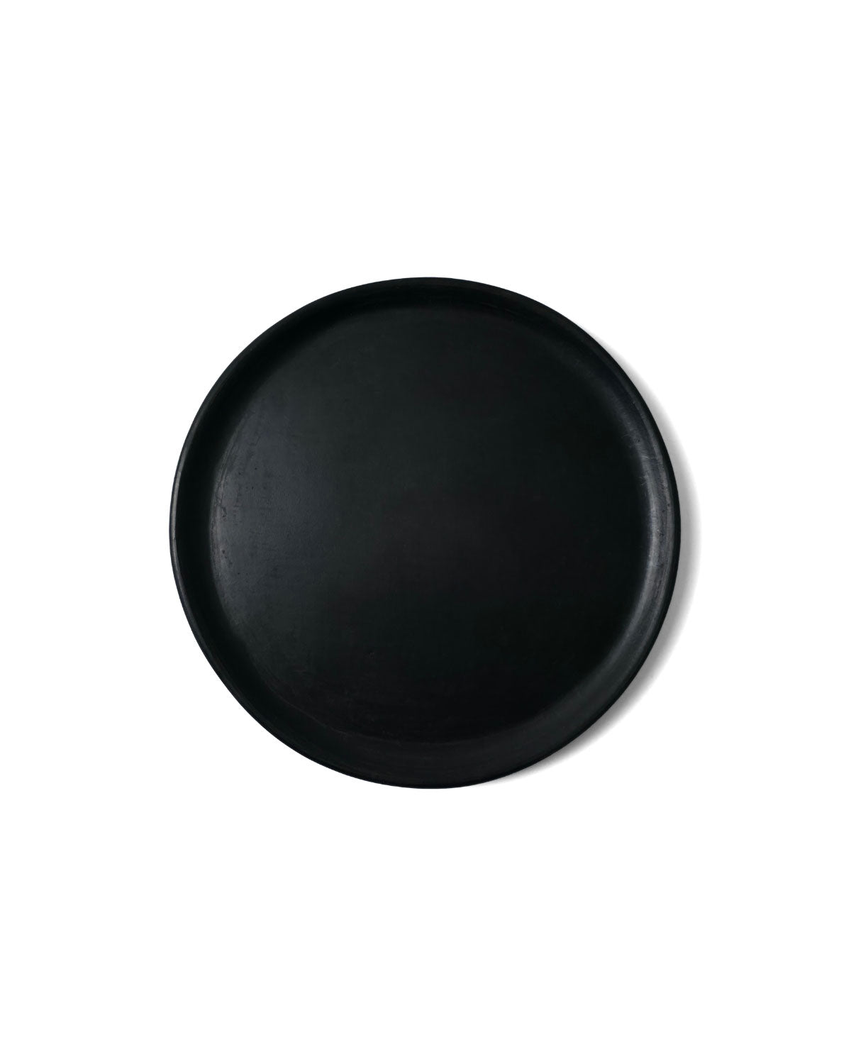 Top view of matte Oaxacan black clay salad plate on white background.