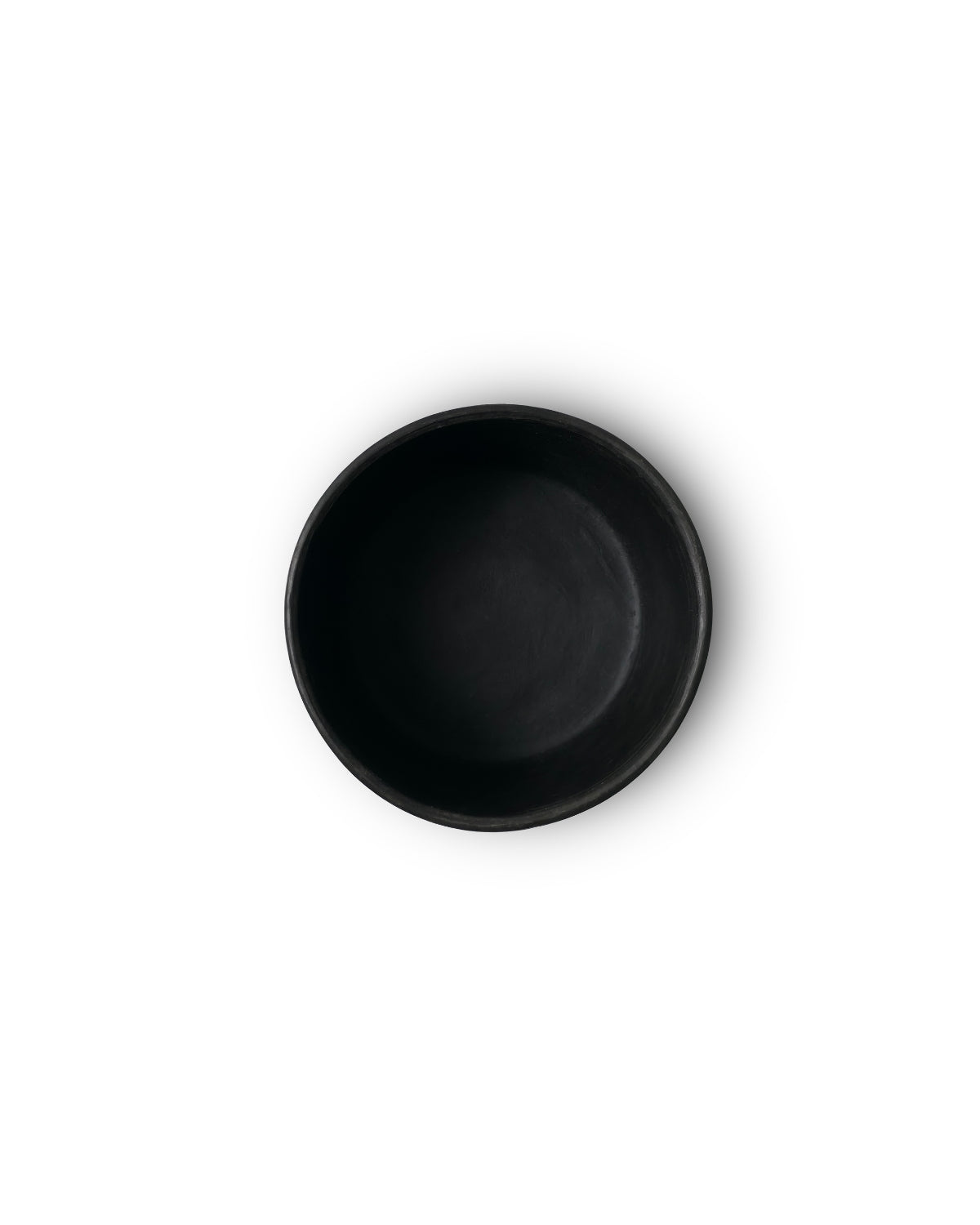 Top view of matte Oaxacan black clay salsa bowl on white backdrop.