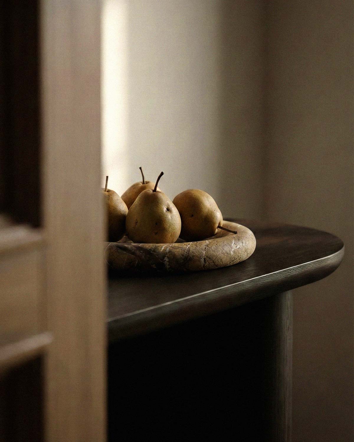 Three pears on a brown marble tray on a wooden surface with a neutral background