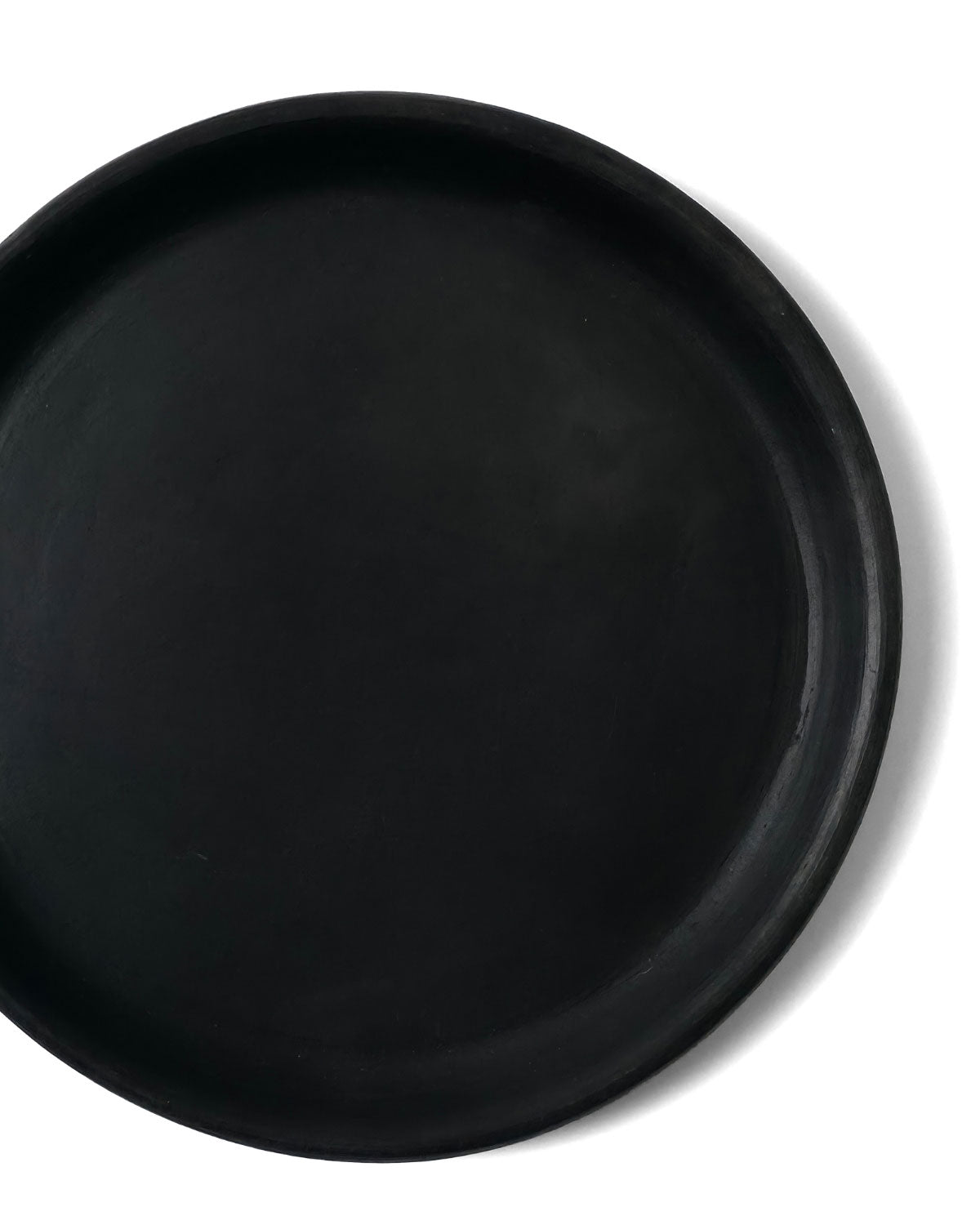 Close-up top view of Oaxacan black clay appetizer plate showing raised rim on white background.