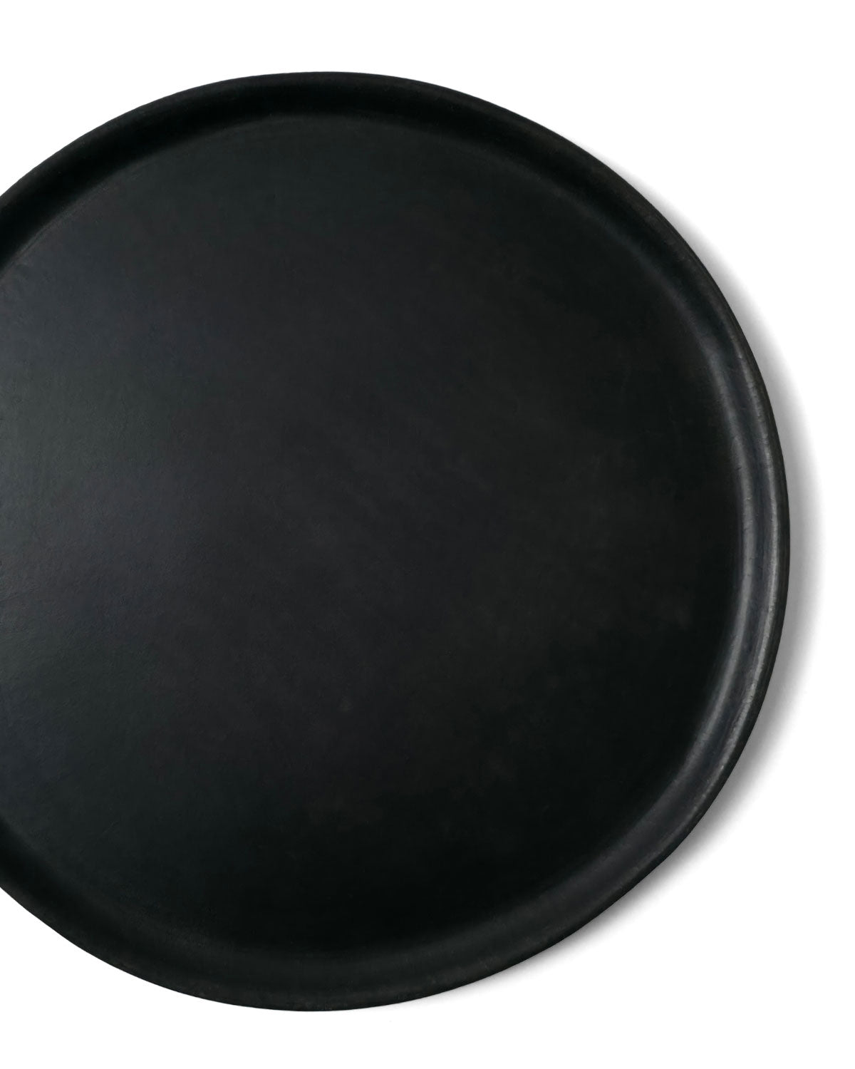 Close-up top view of Oaxacan black clay platter showing raised rim on white background.