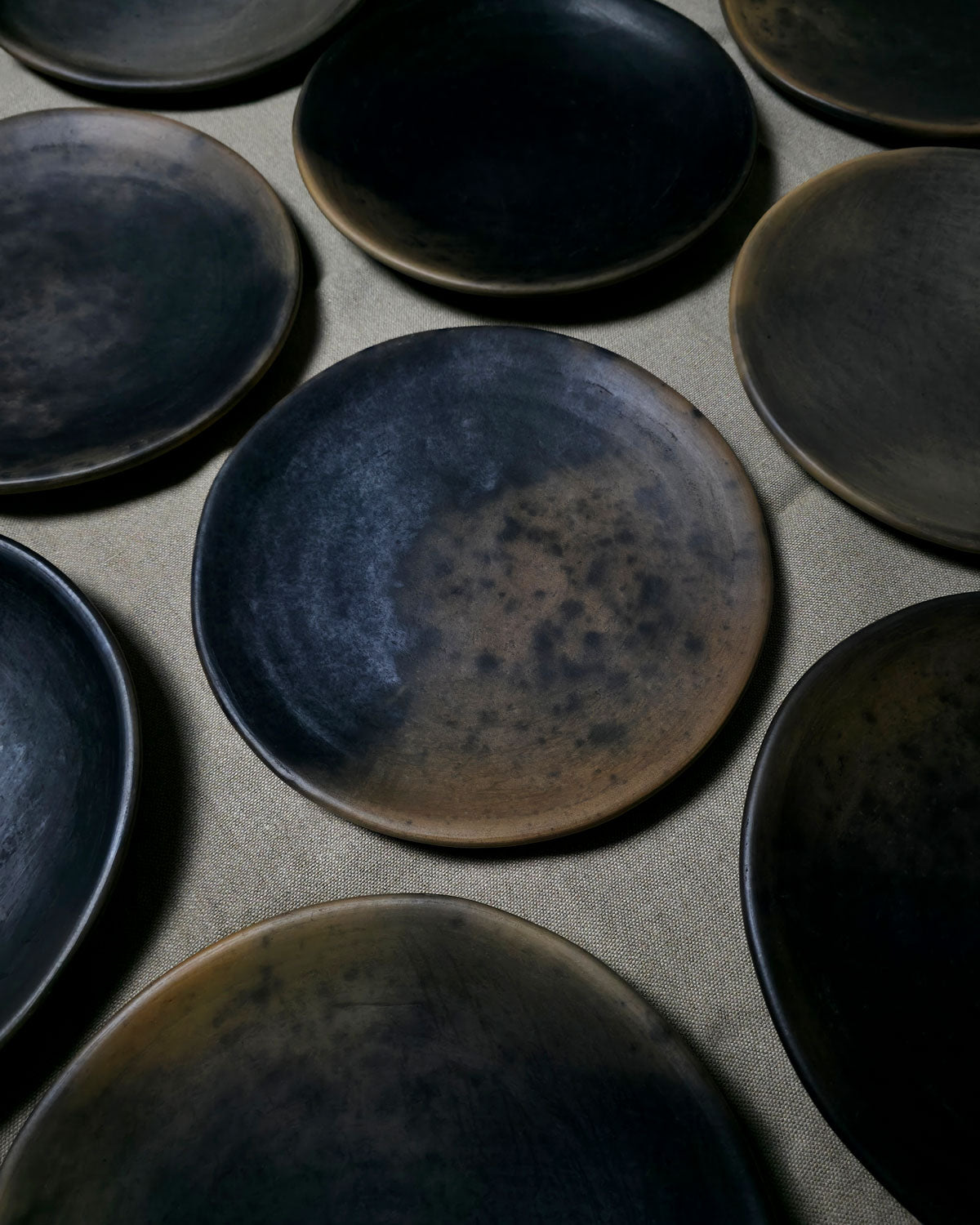Angled view of handmade Oaxacan plates highlighting their rimless curved shape and smoky finish.